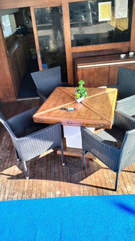 Shalimar IV Tavolo quadrato in legno con quattro sedie attorno, pianta decorativa al centro.