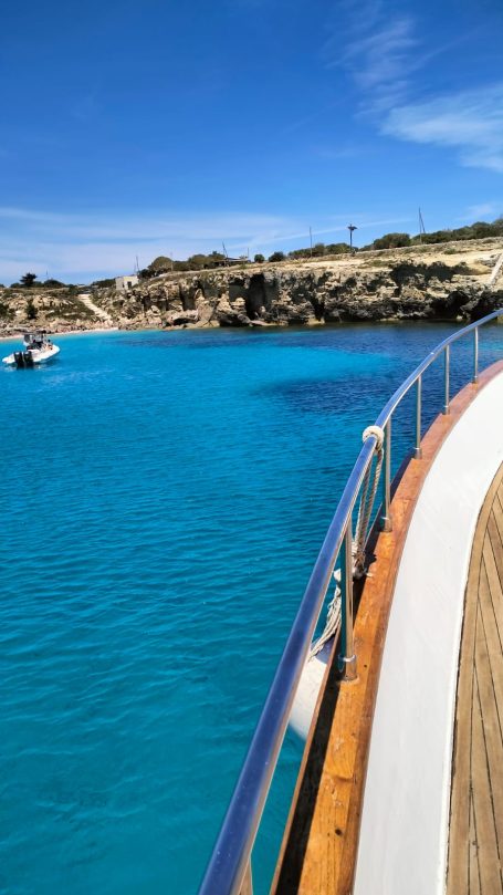 Favignana Cala Azzurra View of a turquoise sea from a boat with rocky shores in the background.