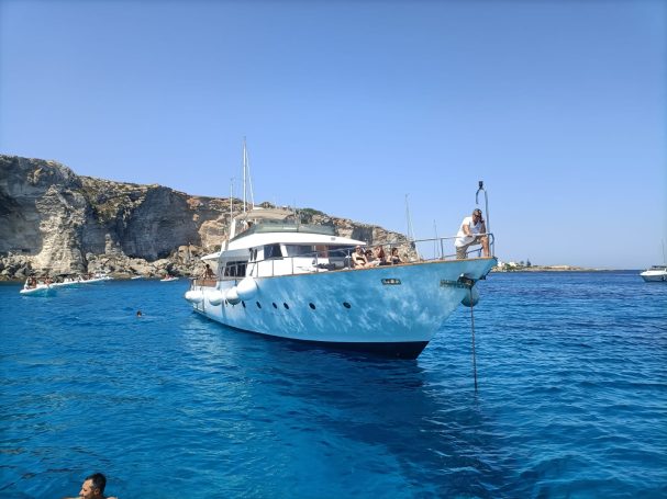 Yacht Shalimar IV Yacht anchored near rocky cliffs in clear blue waters under a sunny sky.