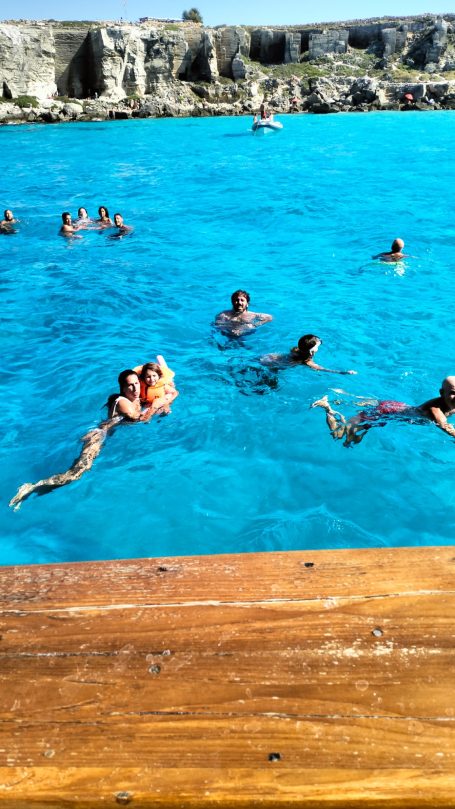 Favignana sosta bagno Persone che nuotano in acqua turchese vicino a una riva in legno.