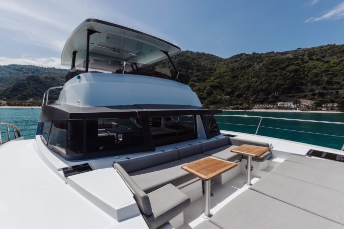 Catamarano Cockpit of a modern yacht with sleek design and two small tables. Scenic waterfront backdrop.