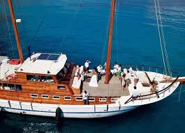 Caicco Traditional wooden sailing boat with crew on deck, moored in clear blue waters.