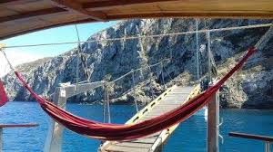 Caicco Amaca rossa appesa su una barca con vista su scogliere e acqua blu.